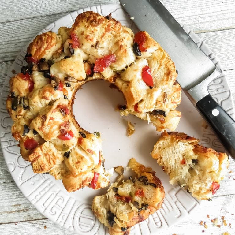 A bundt style loaf of Savory Monkey Bread, Two Ways on a gray plate and a knife to slice.