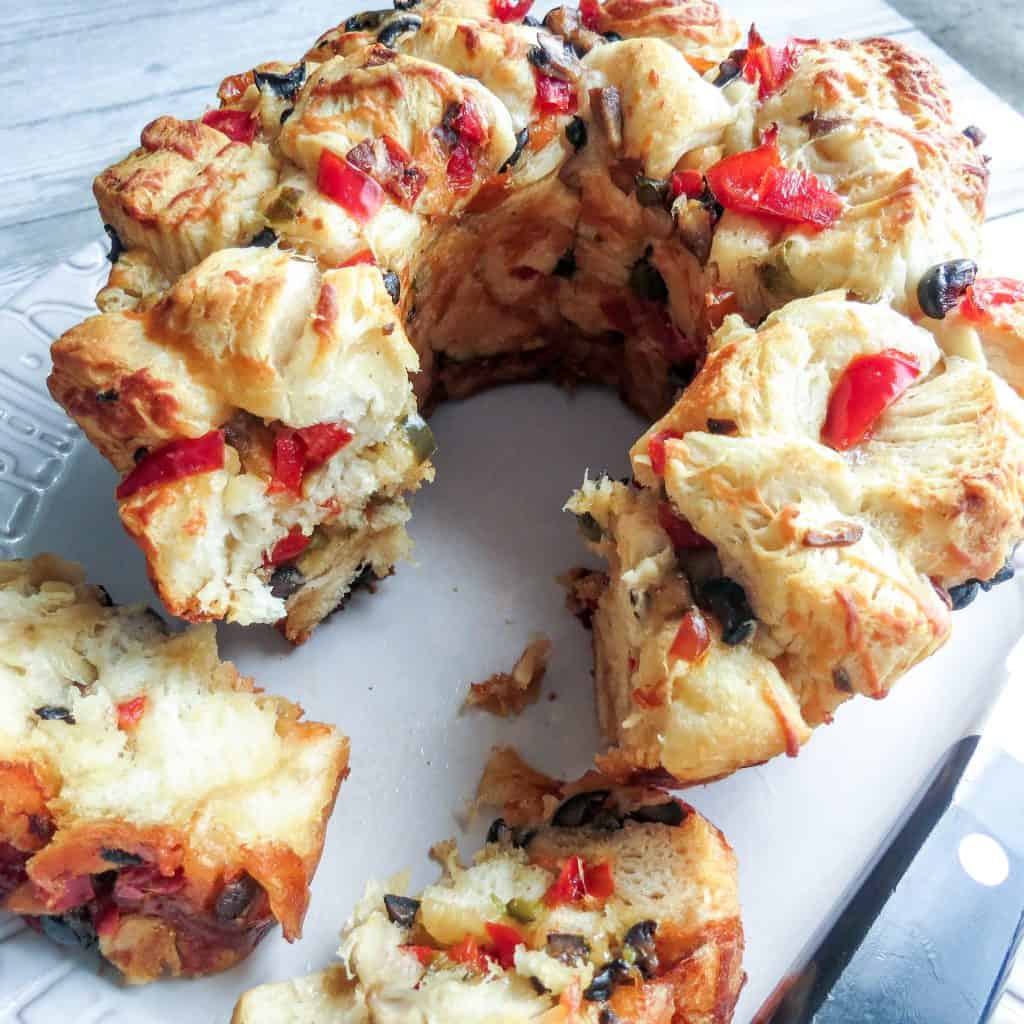 A bundt style loaf of Savory Monkey Bread. Two Ways on a gray plate and a knife to slice.
