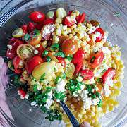 Glass bowl full of Corn Salad With Tomatoes stirred with a silver spoon.