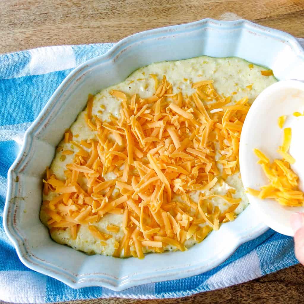 Cheese being sprinkled onto a blue oval casserole dish on a blue and white plaid towel.