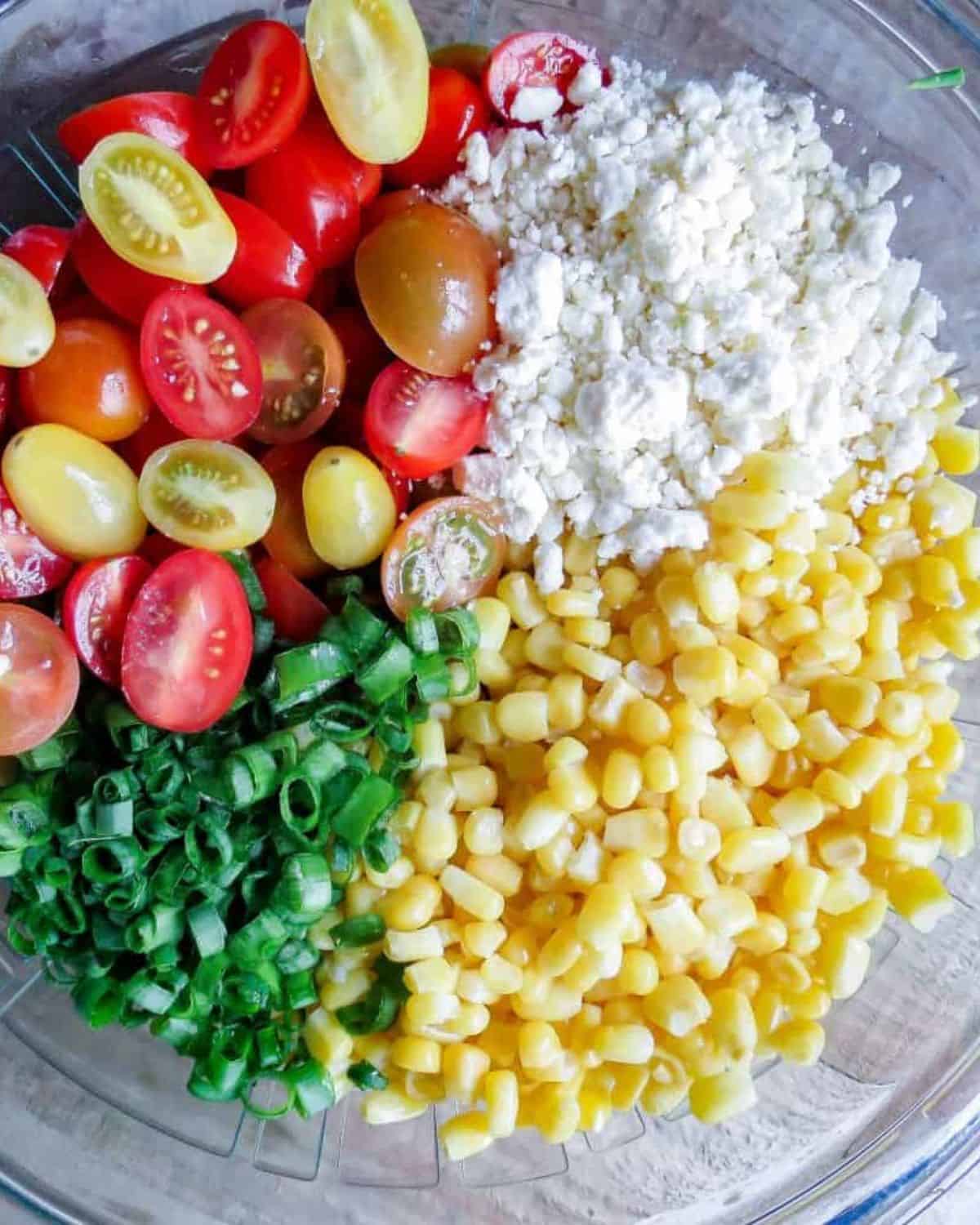 A glass bowl full of ingredients for Corn Salad With Tomatoes.