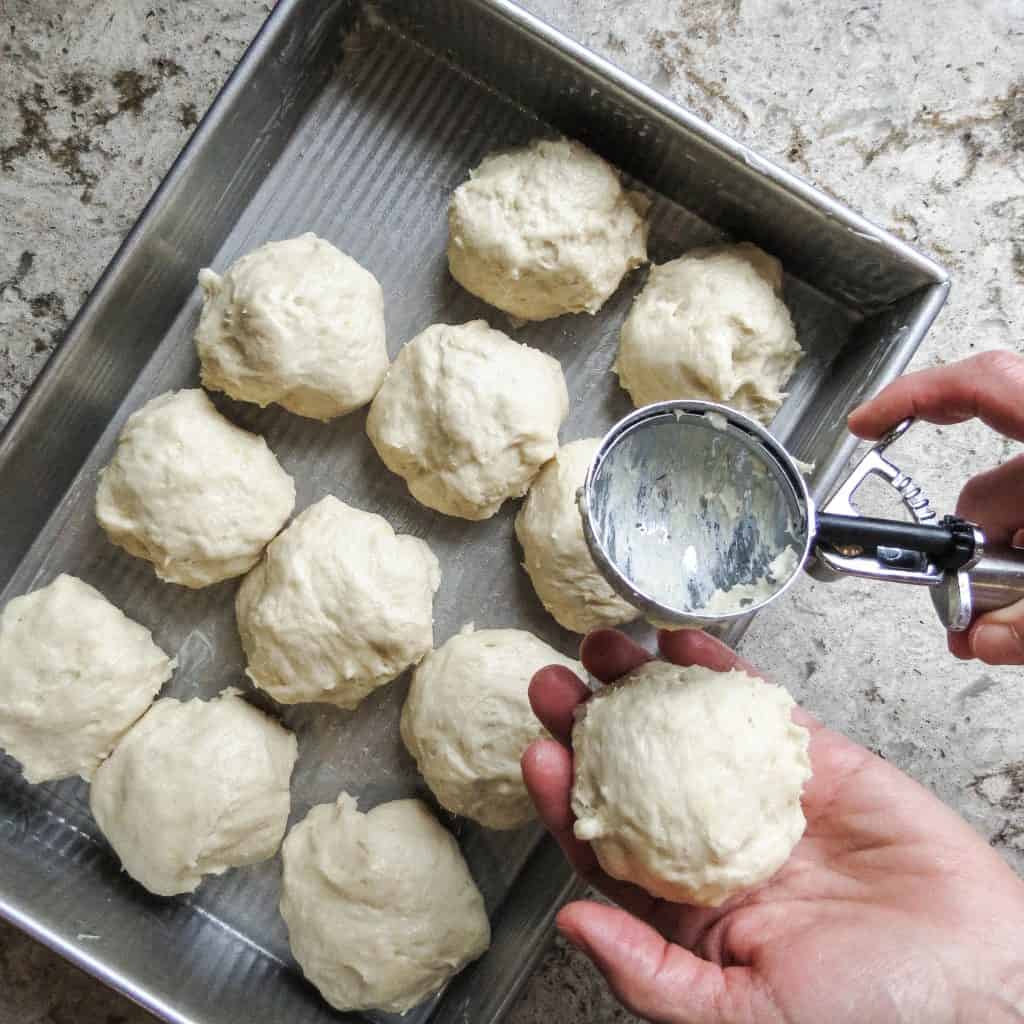 A ball of bread dough from Easy No-Knead Bread with an ice cream scoop onto a pan of unbaked rolls.