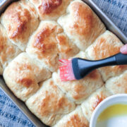 A pastry brush brushing melted butter onto a pan of baked Easy No-Knead Bread rolls.