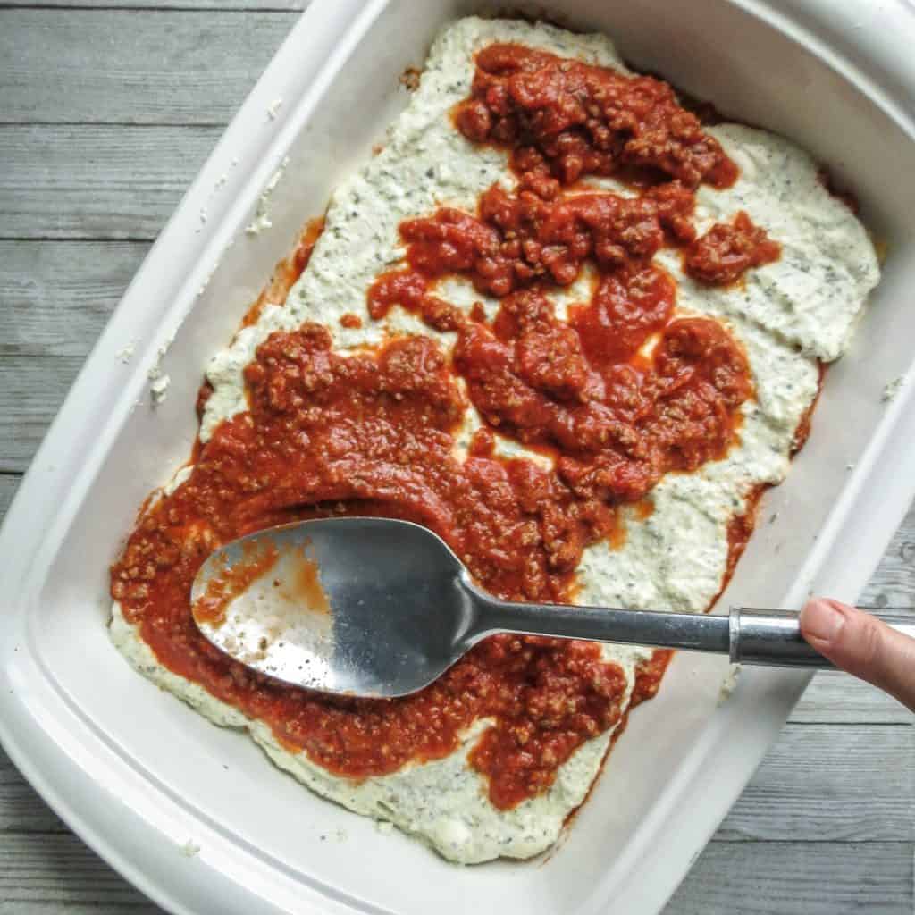 A white casserole dish with layer of sauce on ricotta filling. 