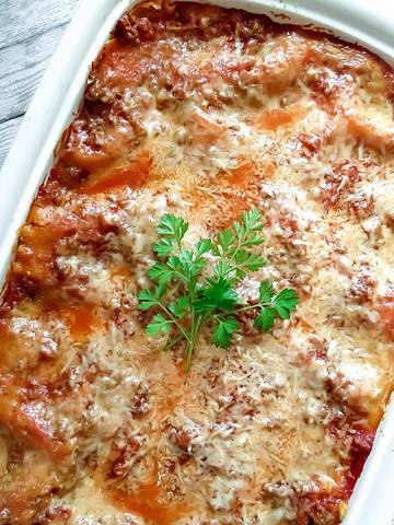 A white casserole dish with a cooked Easy Lasagna Recipe, Step-By-Step garnished with fresh parsley in the center.