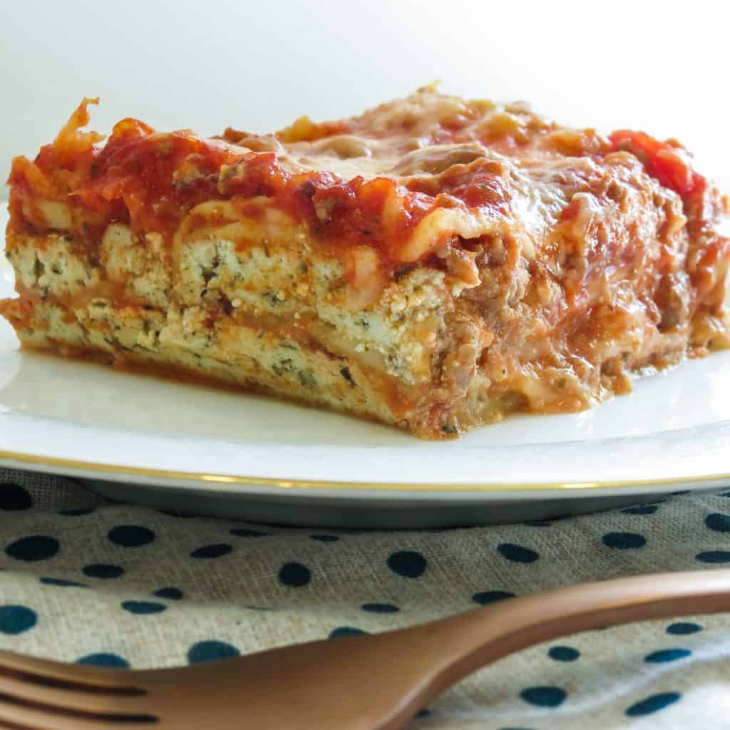 A serving of Easy Lasagna Recipe, Step-By-Step on a white plate on a blue and white napkin.