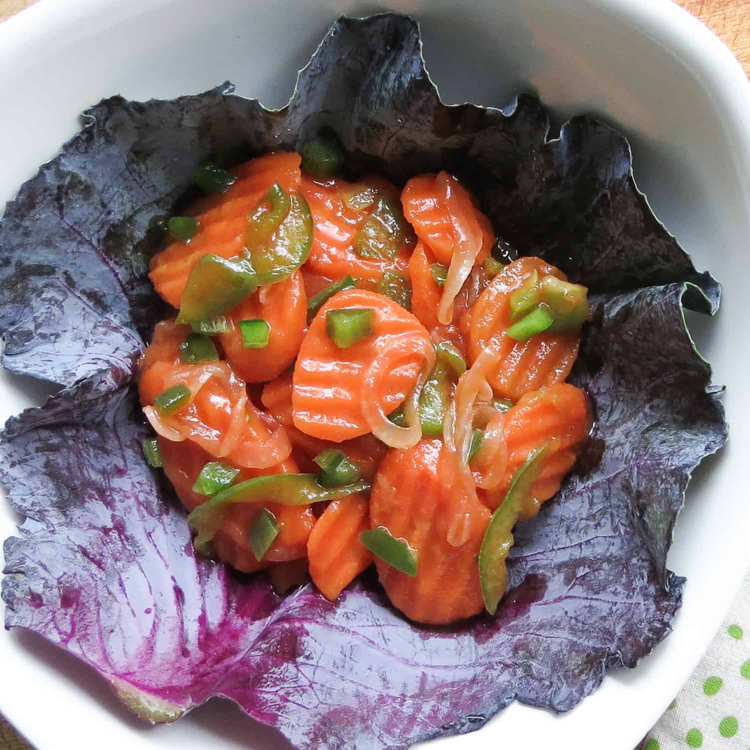 A white bowl lined with a leaf of purple cabbage filled with Copper Pennies Salad With Jalapeños.