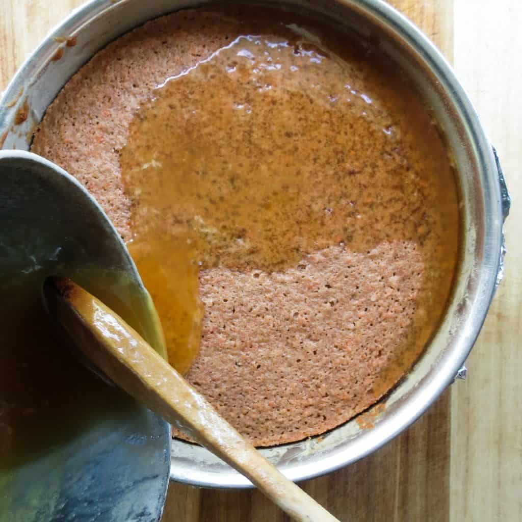 Glaze being poured from a pot onto a cake in a round springform pan.
