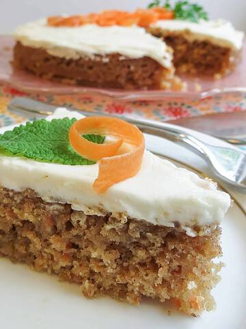 A slice of single layered Glazed Carrot Cake topped with a carrot curl and mint leaf on a white china plate.