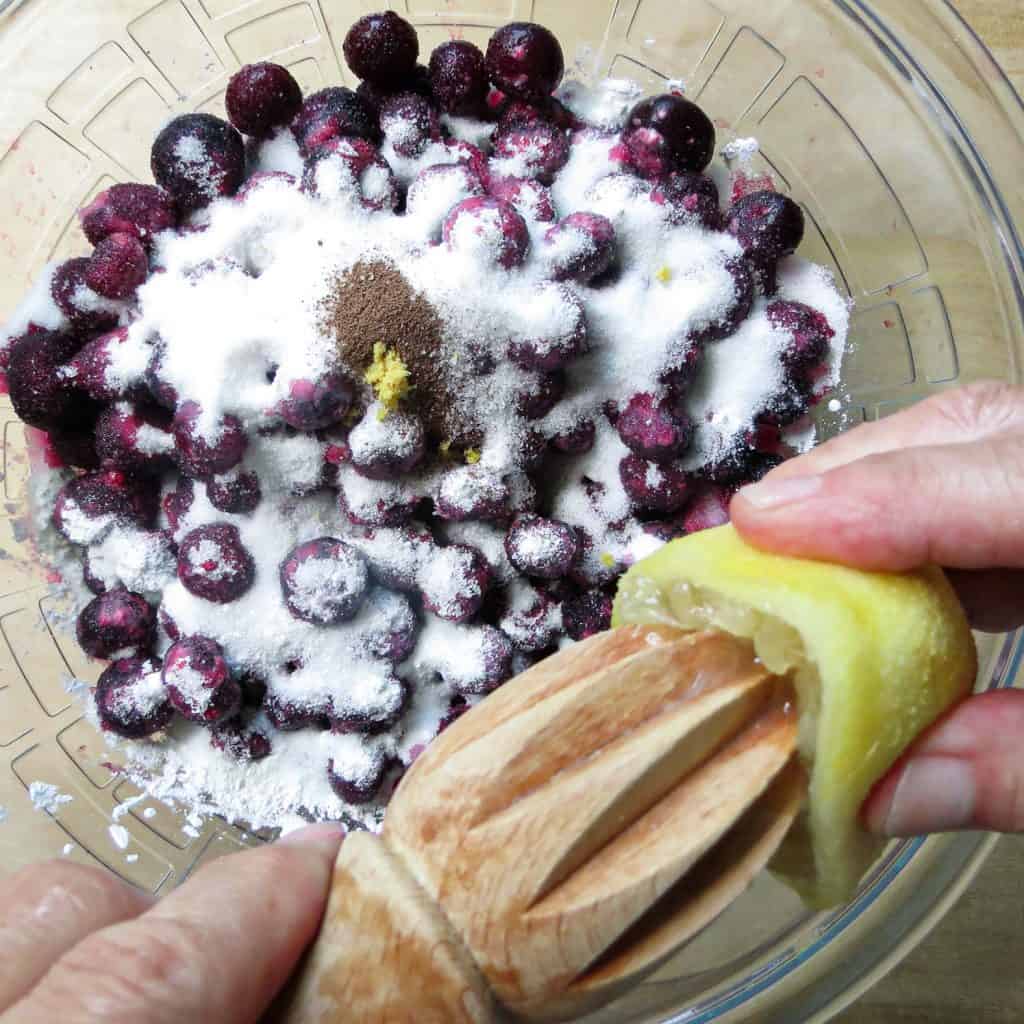Juicing a lemon into a bowl blueberry pie ingredients.