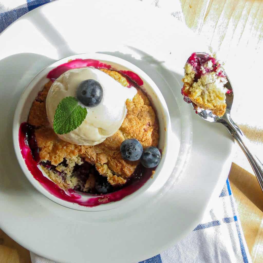 Easy Blueberry Pot Pie in a white ramekin bowl toped with ice cream next to a spoonful of pie.