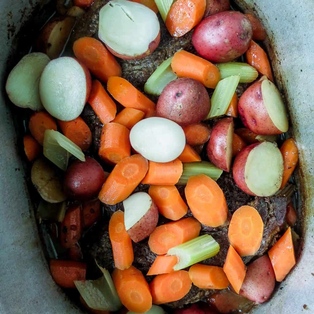 Sliced carrots, potatoes, and celery on top of a large pot of roast beef and gravy.