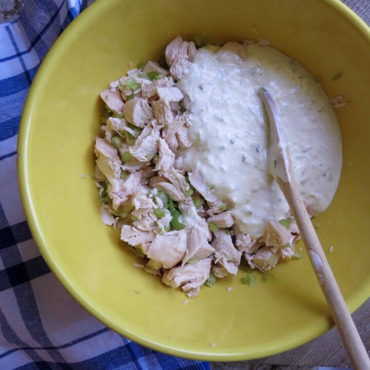 A yellow bowl of chicken and celery with a wooden spoon stirring in a creamy white dressing.