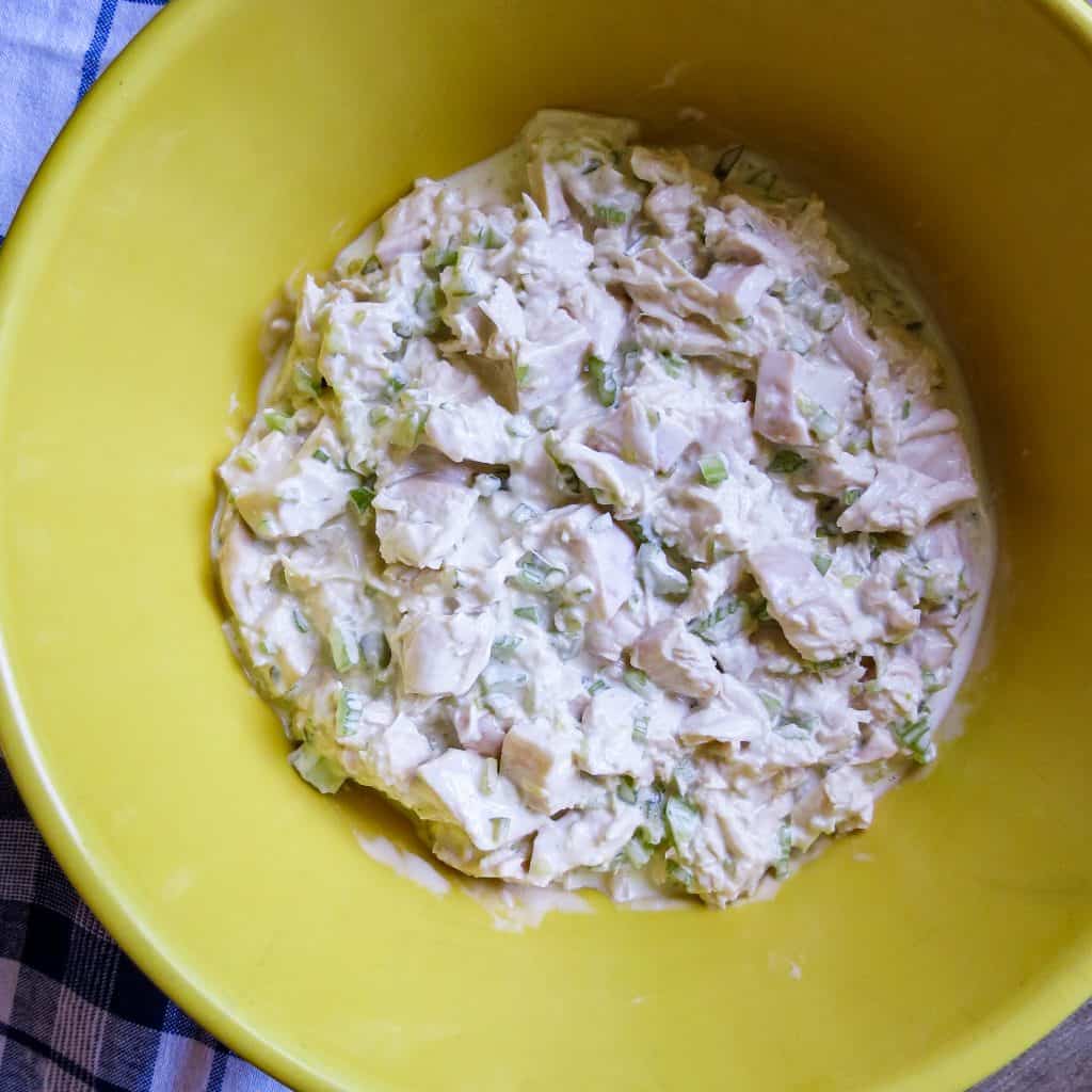 A yellow bowl of Chicken Salad Your Way on a blue and whit cloth.