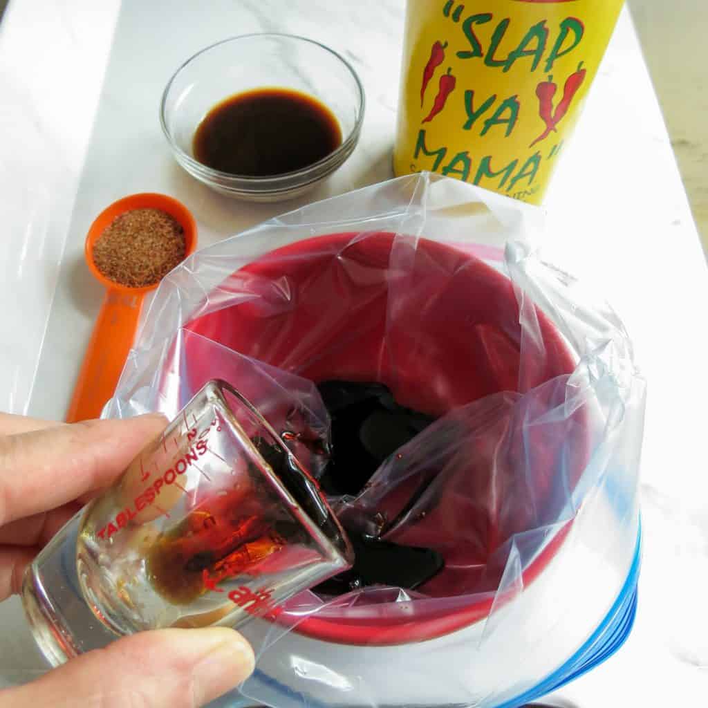 Sauce being poured into a ziplock bag in a red bowl with a can of Slap Ya Mama seasoning for Marinated Hot Dogs.