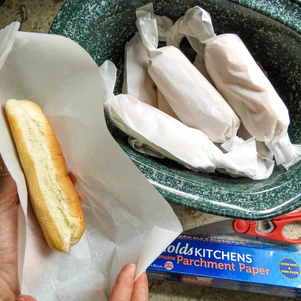 Buns wrapped in parchment paper stacked in a crock pot.