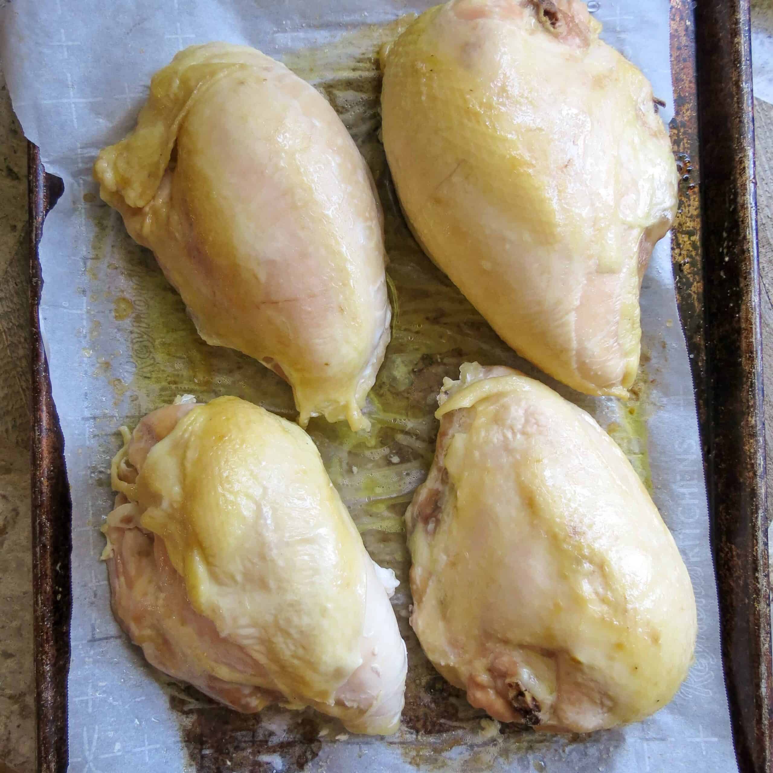 Four roasted bone-in chicken breasts laying on a piece of parchment paper on a sheet pan.