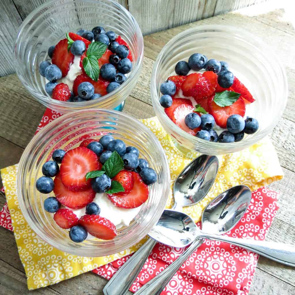 Three glass dessert cups with strawberries and blue berries on top of cream filling for Keto Lemon Berry Dessert.