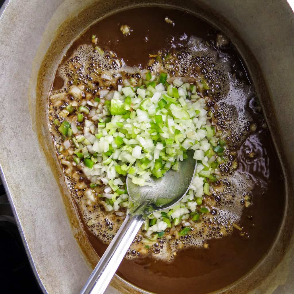 A silver pot of dark roux with chopped onions, bell peppers, and celery stirred into.