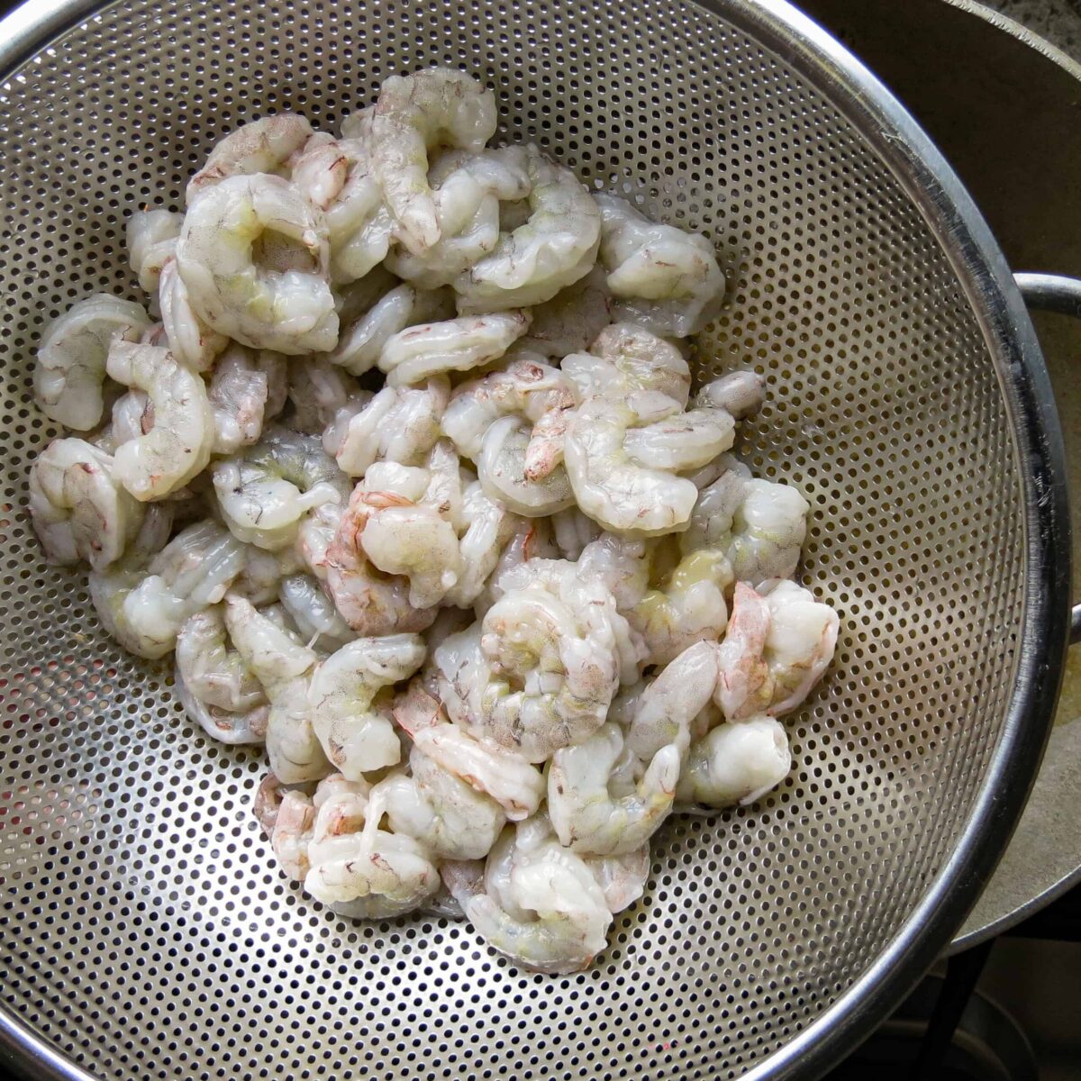 A silver drainer with fresh shrimp in it.