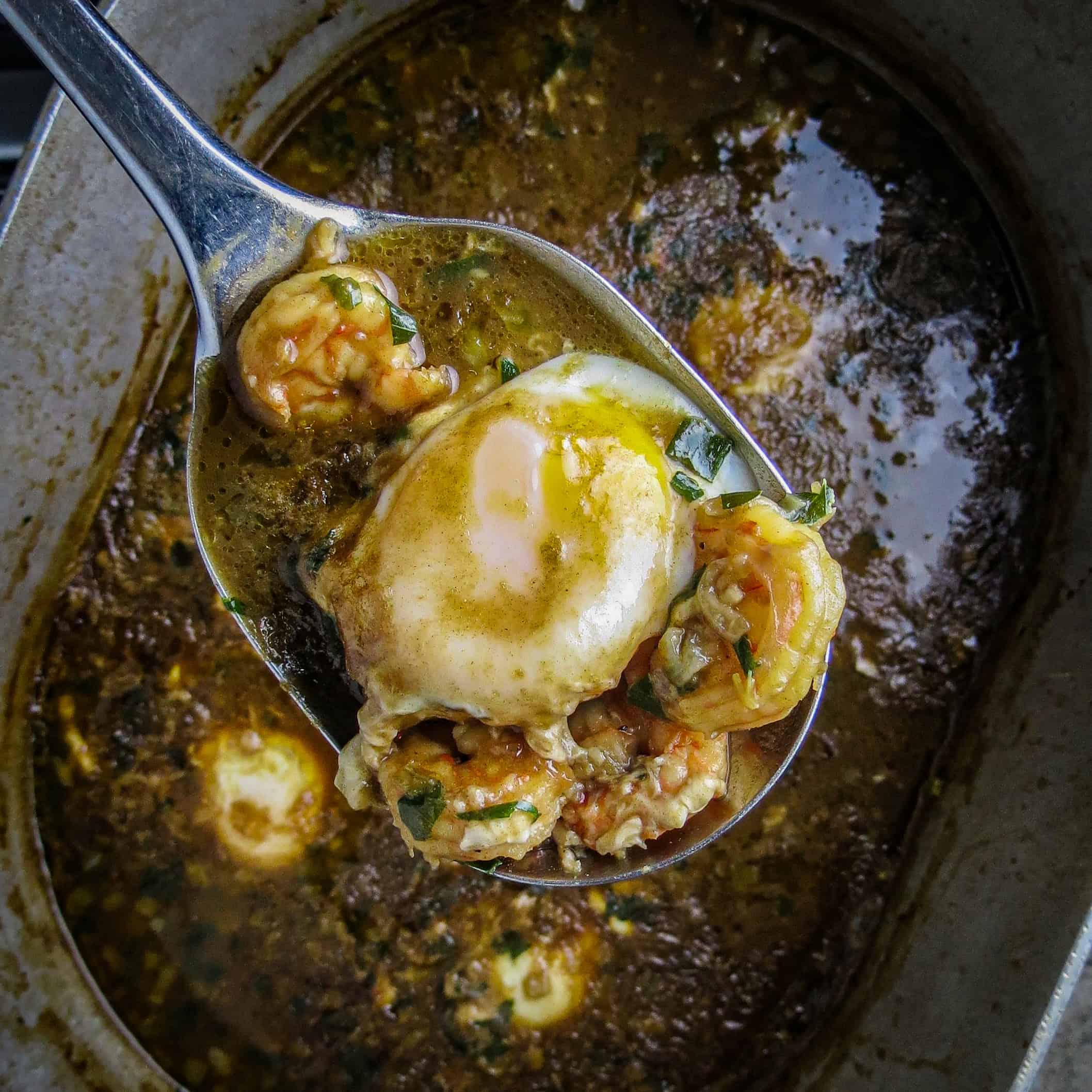 A pot of shrimp and egg stew with shrimp and poached egg ladled in a spoon over the pot.