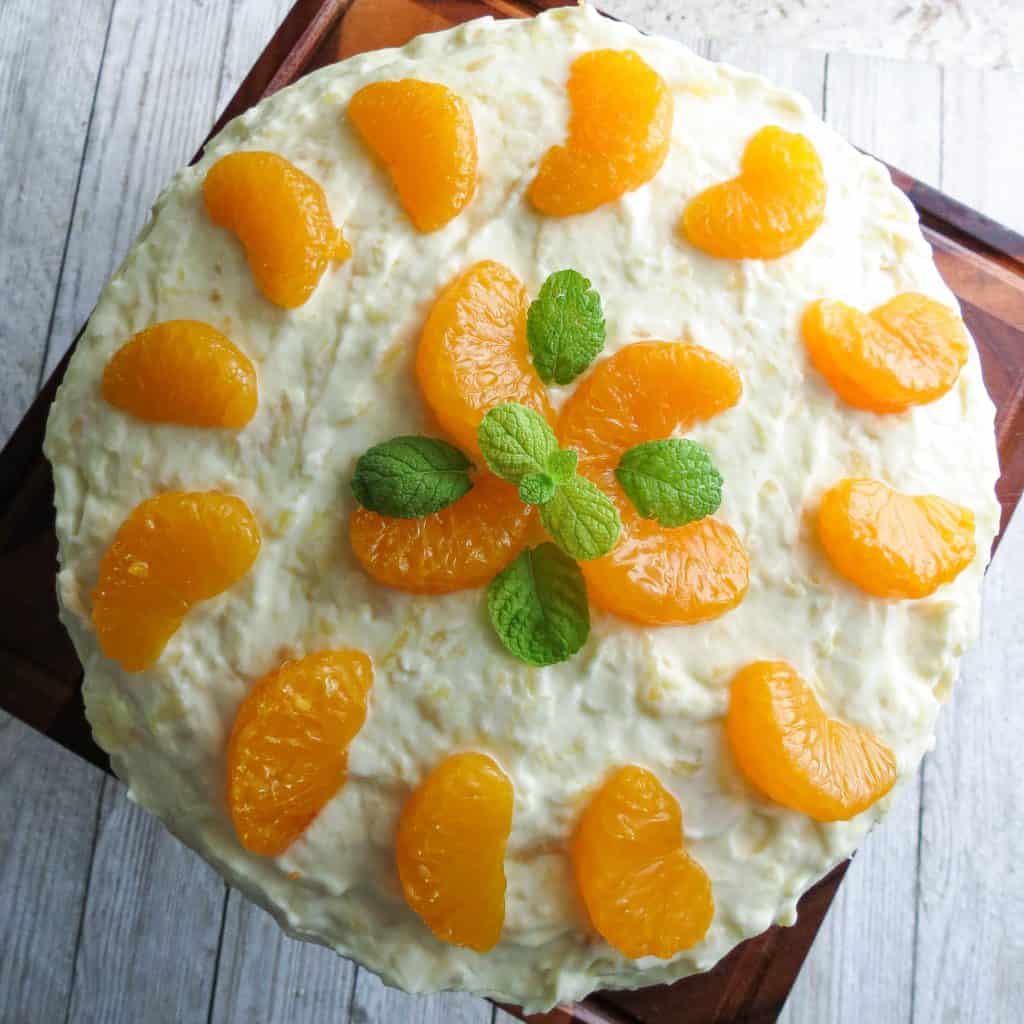 A round white cake topped with a mandarin orange design with mint leaves resembling a flower.