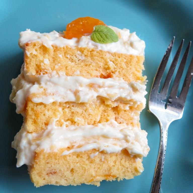 Slice of 3 layer Mandaliscious Mandarin Orange Cake on a blue plate with a fork.