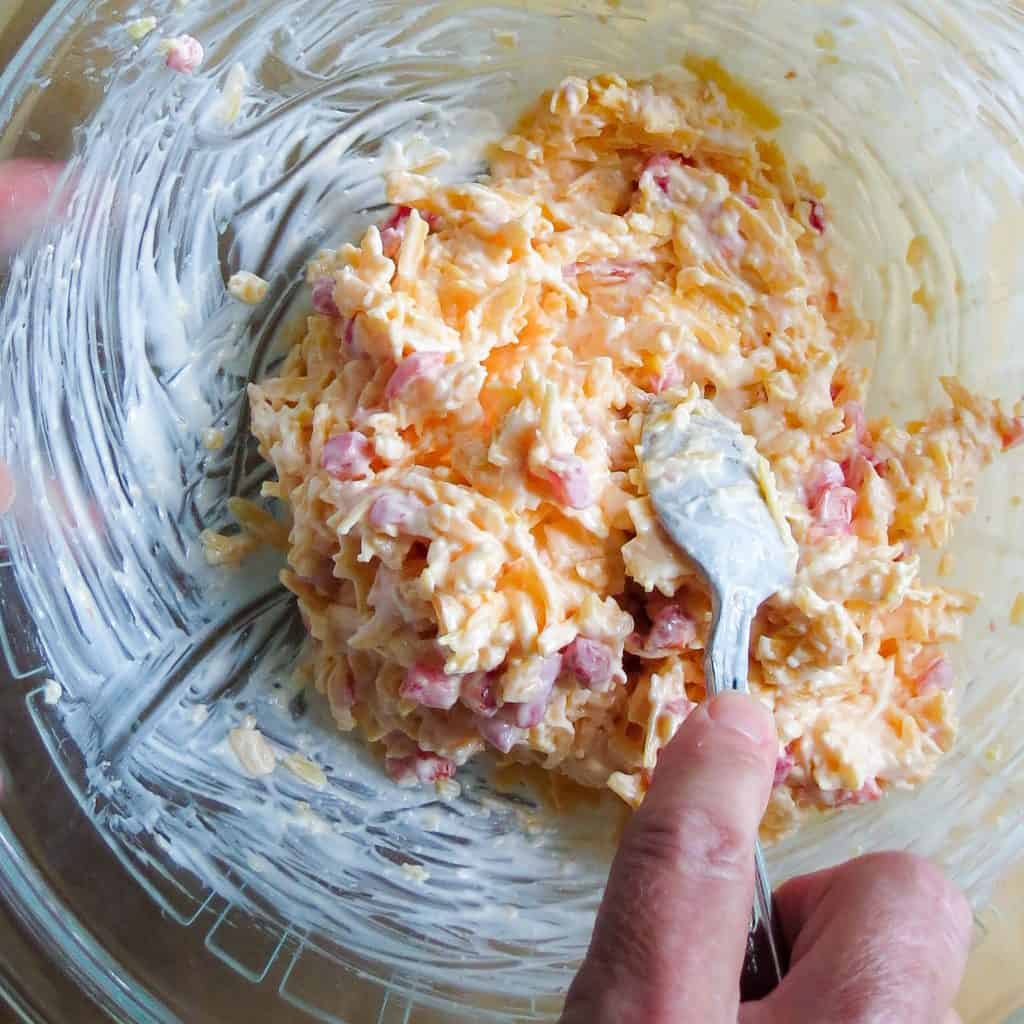 A glass bowl with a hand stirring its ingredients.