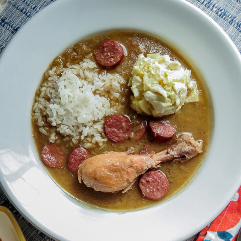A white bowl of chicken and sausage gumbo with rice and a scoop of Plain Potato Salad in it.