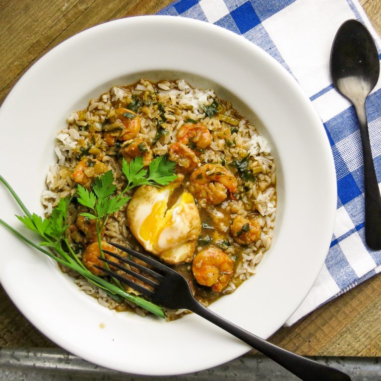 A white bowl of shrimp stew on rice with a poached eggs cut into with a fork.