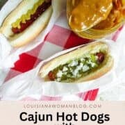 Two dressed hot dogs with a jar of sauce on a red and white checked tablecloth.