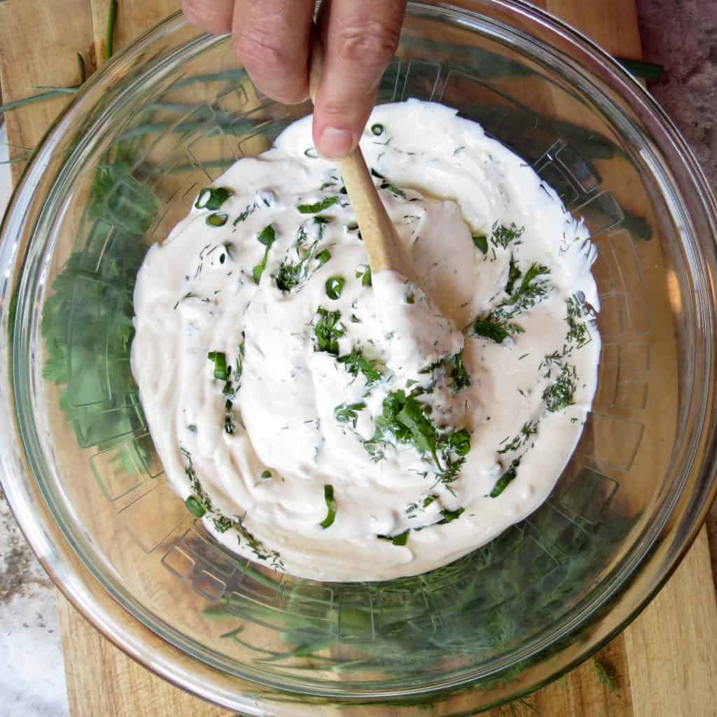 A glass bowl of Fresh Herb Dip with a wooden spoon stirring its ingredients.