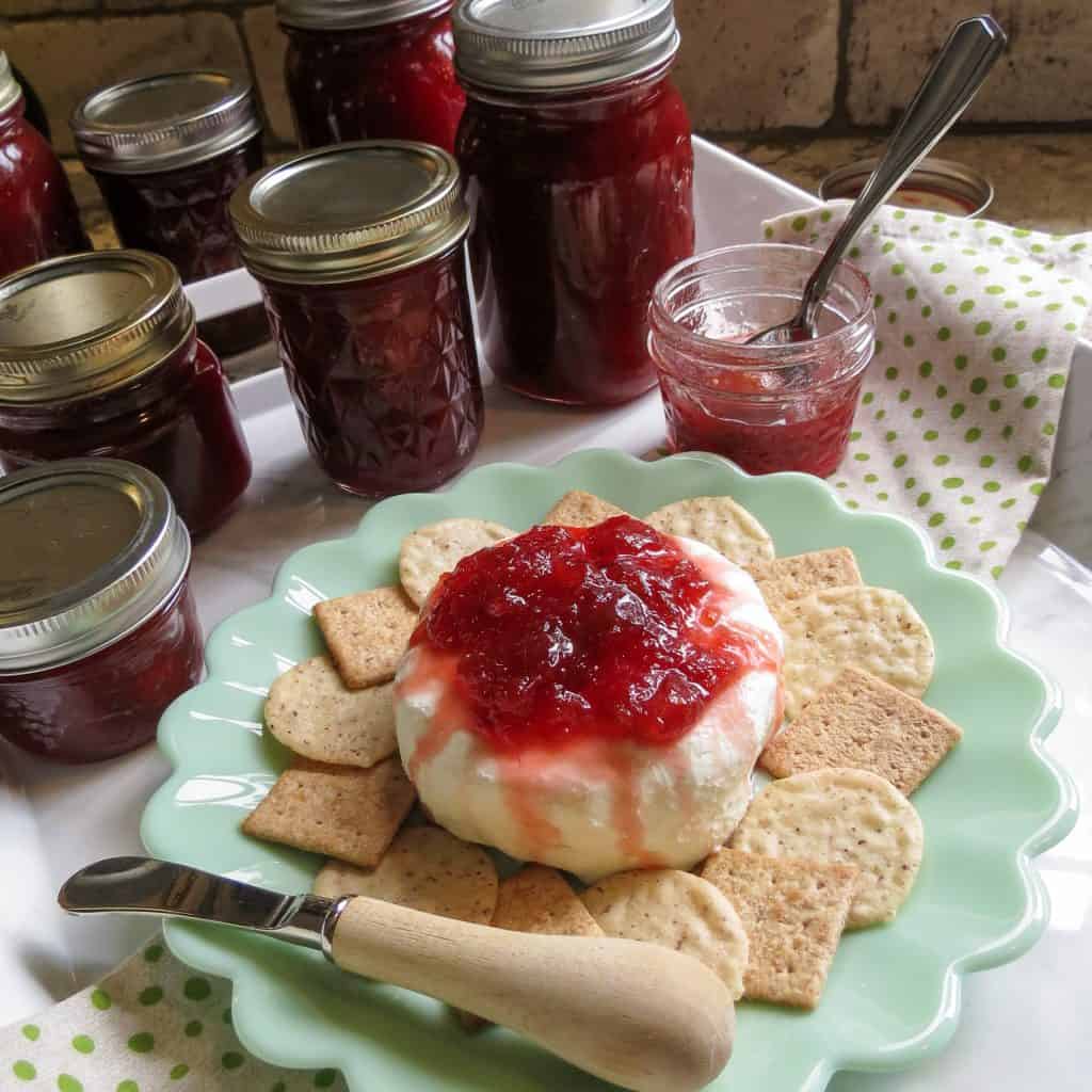 Jars of fig jam with a plate of crackers and cream cheese topped with fig jam.
