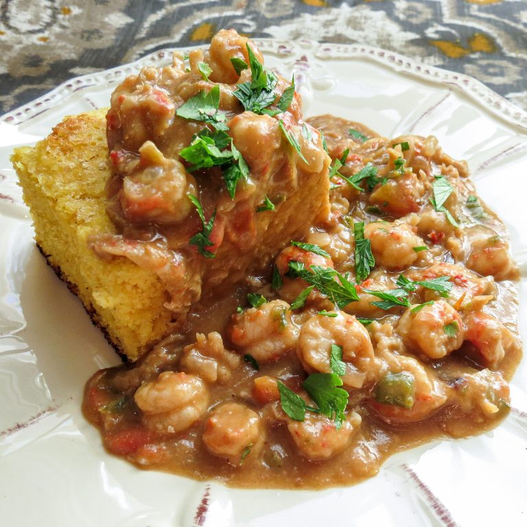 A dish of a square of cornbread topped with a crawfish stew.