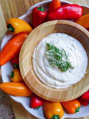 A bowl of Fresh Herb Dip with dill on top with colored peppers around it.