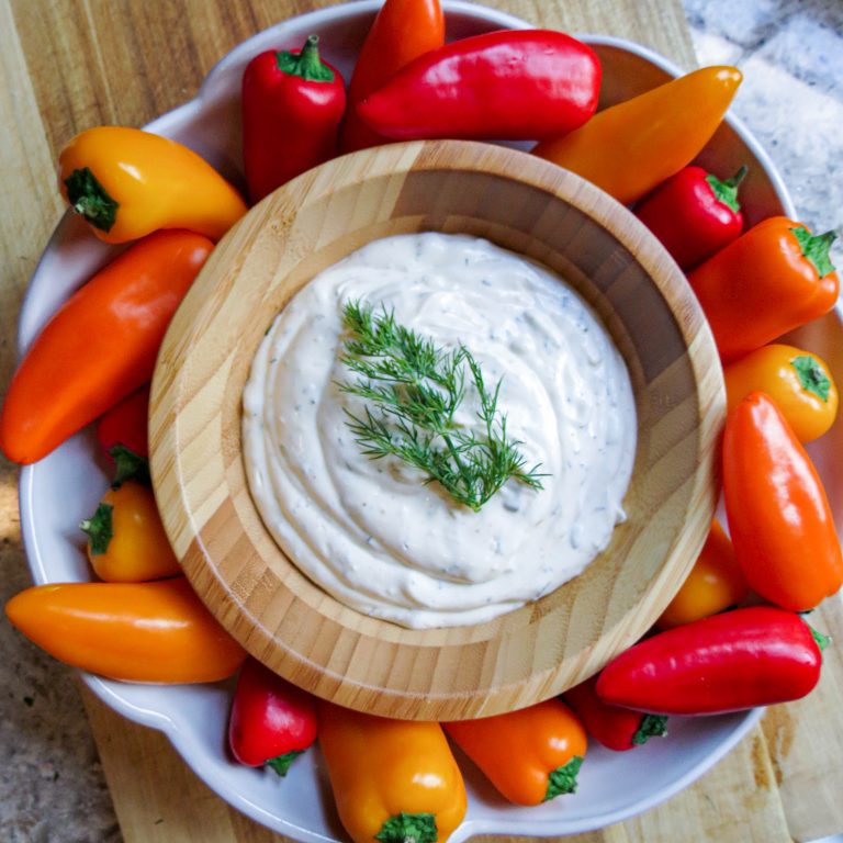 A bowl of Fresh Herb Dip with dill on top with colored peppers around it.
