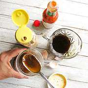 A jar of vinaigrette with some ingredients on a plank board.