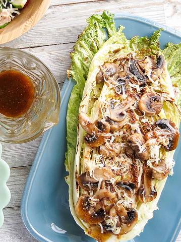 A plate of grilled greens and mushrooms with a dressing on a plank board.