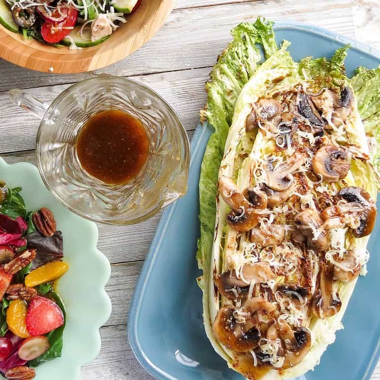 A plate of grilled greens and mushrooms with a dressing on a plank board.