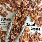 A Pinterest Pin for Buttery Salted Pecans with pecan halves spread out on a parchment paper with kitchen tongs scooping them up.