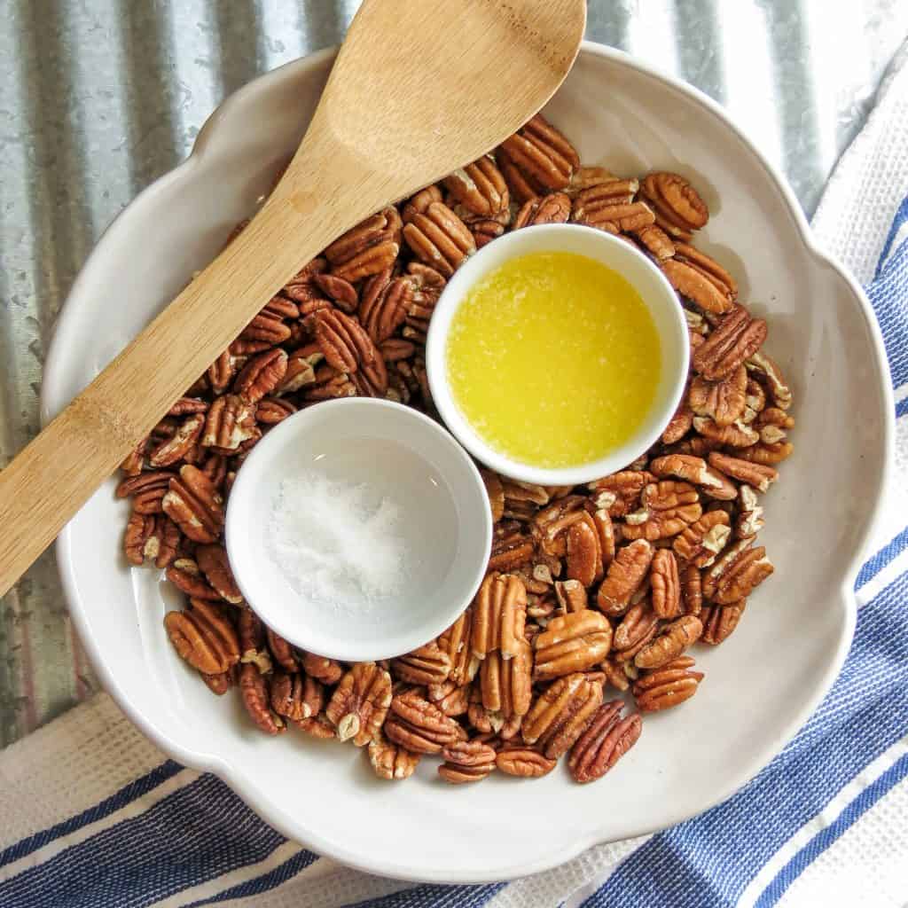 A bowl of pecans with a spoon and ingredients of butter and salt.