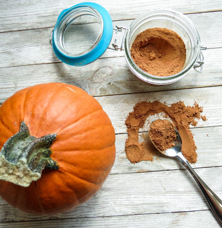 Jar of spice mix with a small pumpkin and a spoonful on a board.