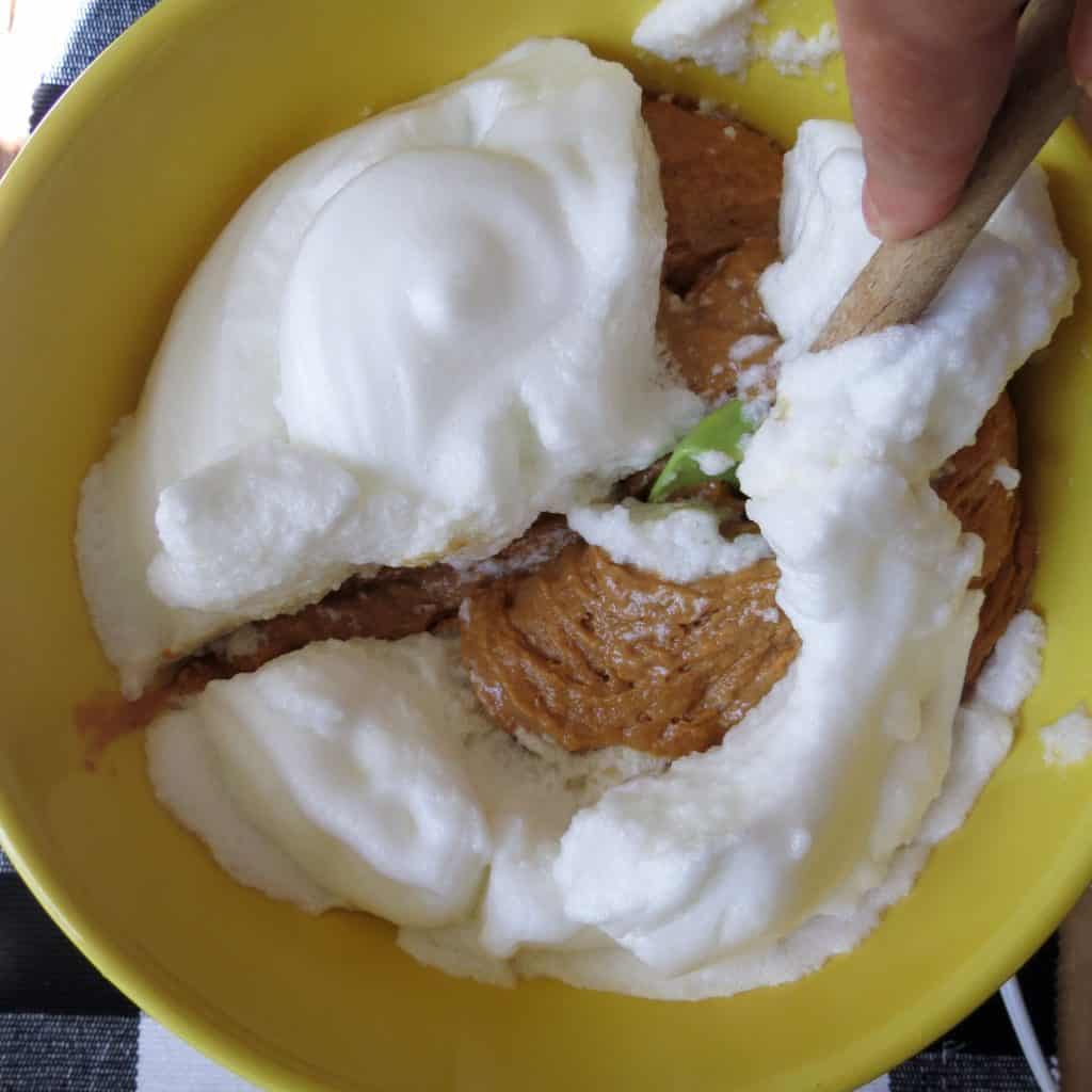 A yellow bowl with egg whites being folded onto batter with a spoon.