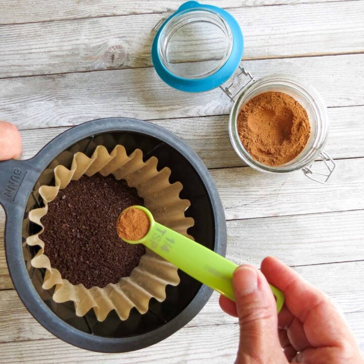 Basket of coffeemaker with coffee and a spoonful of spices being added.