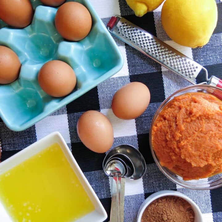 Eggs, pumpkin, lemons, melted butter and spices on a black and whit buffalo checked cloth.