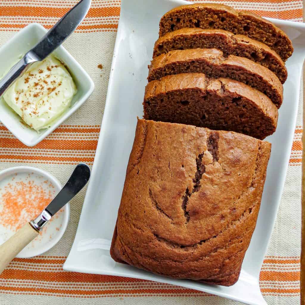 A loaf of sliced pumpkin bread with a bowl of butter and icing beside it.