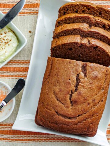 A loaf of sliced pumpkin bread with a bowl of butter and icing beside it.