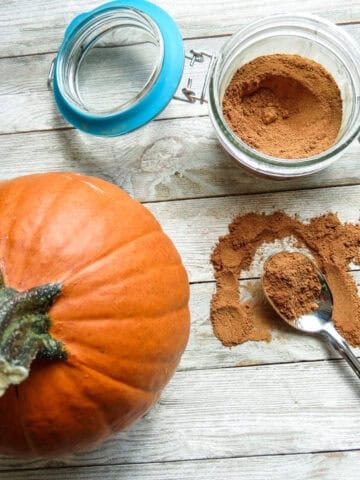 Jar of spice mix with a small pumpkin and a spoonful on a board.