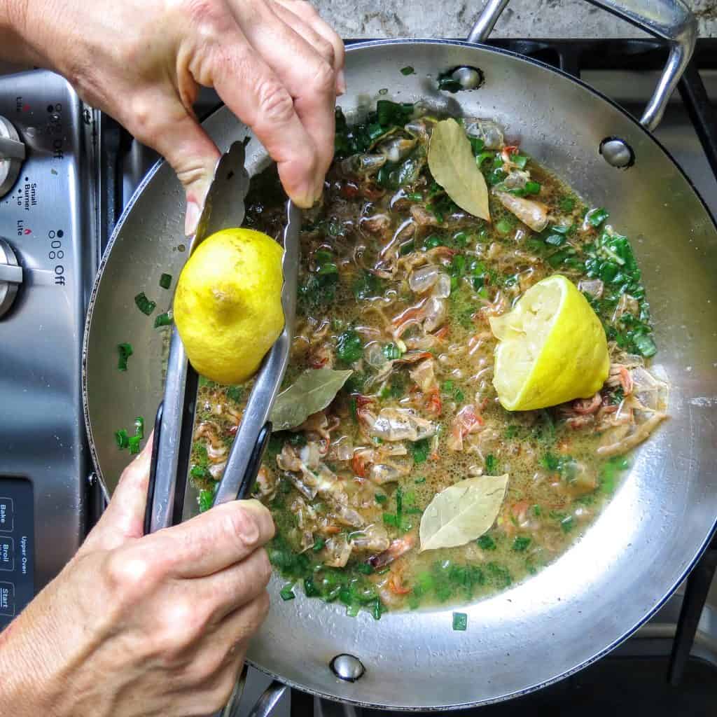 Lemons being squeezed into a saucepan of barbecue shrimp sauce.