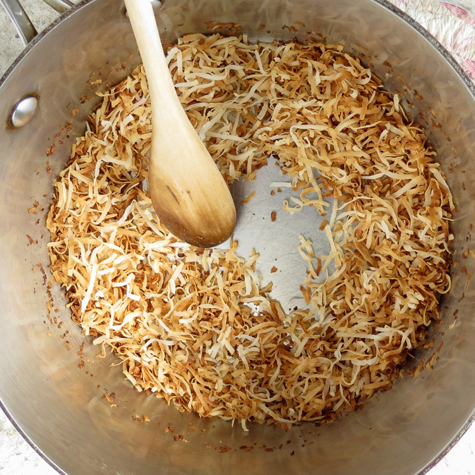 A wooden spoon stirring shredded coconut in a sauce pan.